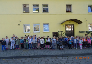 Dzieci z rękawiczkami na rękach stoją przed budynkiem przedszkola.